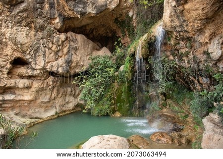 Natural setting with an emerald-colored pool at the foot of a small waterfall in the town of Yátova. Cueva de las Palomas in the Hoya de Buñol-Chiva. Natural pool and caves.