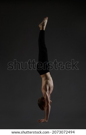 Athletic young guy performs a handstand isolated on a dark background.