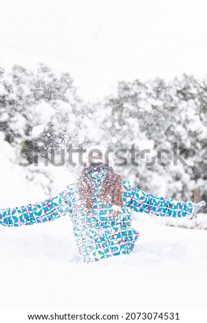 Young woman, having fun while throwing snow in the air, during a walk in a snowy forest, vertical shot