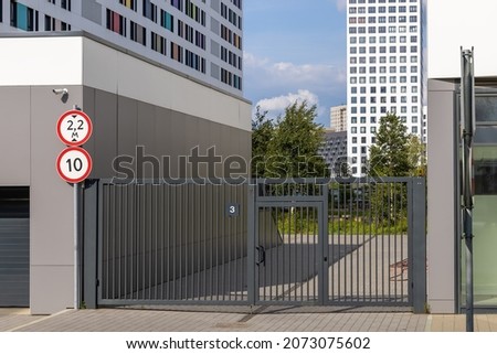 Entrance to the courtyard of a modern multi-storey residential complex. Lattice gates with a wicket and an entrance portal to the underground parking. Residents safety concept. Royalty-Free Stock Photo #2073075602