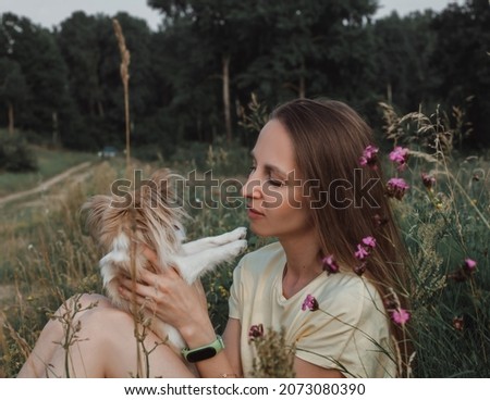 Portrait of a Young woman in a yellow T-shirt and denim shorts who holds a light-colored Chihuahua dog in her arms in the summer on a sunny day in the park
