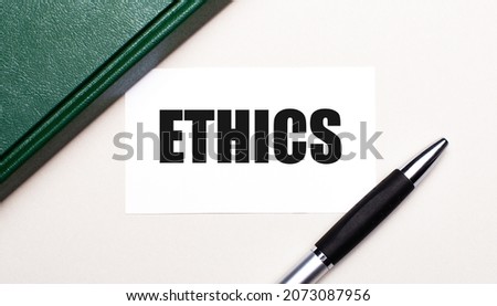 On a light gray background lies a pen, a green notebook and a white card with the text ETHICS. Business concept.