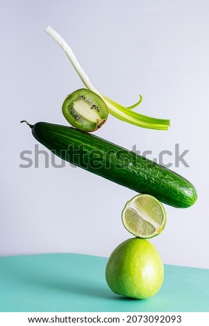 Balance of fruits and vegetables. Apple, lime, cucumber, kiwi and onion on top of each other in a pyramid. Green vegetables and fruits on a white-green background