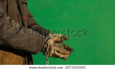a man in dirty clothes with a chain on his hands. gloved hands wrapped in a chain. background picture. the worker asks for payment for labor.