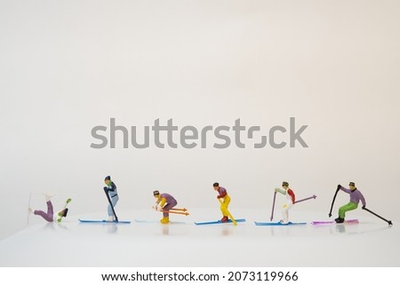 miniature people ride one behind the other on their skis. the first one lies on the ground because of a fall. Skier accident. white background, copy space.
