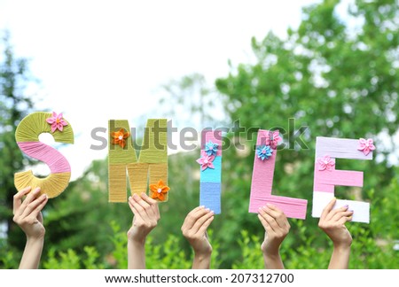 Hands holding up letters building word smile on natural background