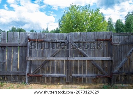 An old wooden gate made of planks, fastened with a wooden crossbar against the background of summer clouds. Soft sunlight.