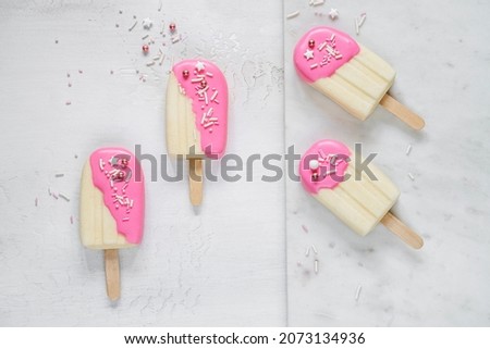 Top table view on four delicious vanilla ice cream bars with pink glaze surrounded by scattered sugar sprinkles on light background. Frozen dessert and summer snack concept Royalty-Free Stock Photo #2073134936
