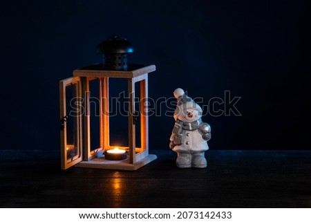 New Year snowman and old lantern with burning candle on dark background.