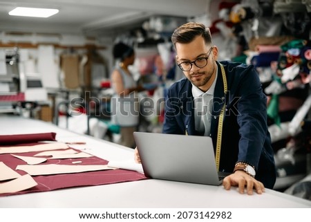 Young clothing designer using computer while working at textile workshop. Royalty-Free Stock Photo #2073142982