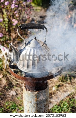 A metal kettle with water is on the wood-burning stove in the garden, the water is boiling.
