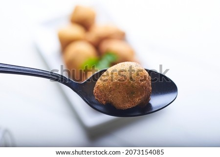 cod fritter on a black spoon with an out of focus background with more fritters on a table