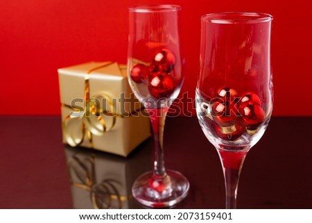 Two champagne glasses with small Christmas balls inside against red background