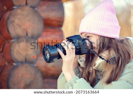 The girl smiles and photographs someone with a camera.