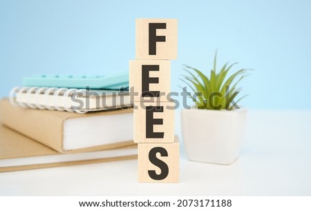 Wooden cubes with letters on a white table. The word is FEES. White background with photo frame, house plant.