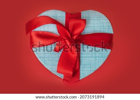 Gift box in the shape of a heart with a red bow on a red background. Gift for valentine's day, new year or mother's day.
