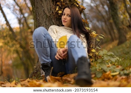 A beautiful girl sits leaning against a tree in the fall, and plays with leaves.