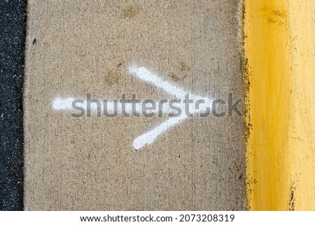 Spray painted arrow on the side of a road pointing to a yellow curb