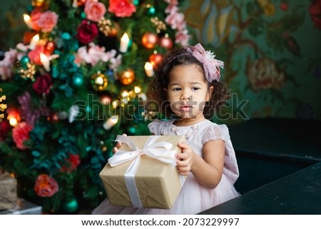 Cute African American little girl with a Christmas gift box or a Christmas gift at home. Celebrating Christmas Holidays, Merry Christmas and Happy Holidays