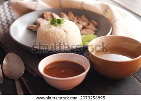 Hainanese chicken rice served with dipping sauce and hot broth on a black wooden table.