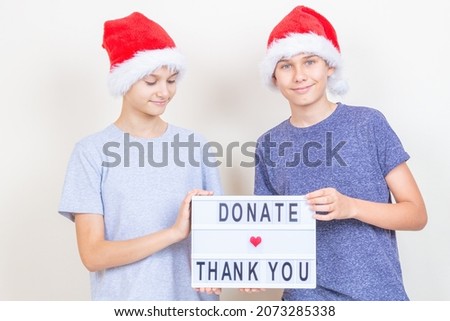 Christmas donation, charity. Teenager boys volunteers with red Santa hat holding lightbox with message Donate and Thank you