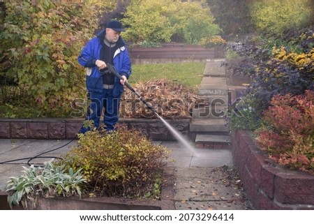 A man washes a garden path with a high pressure washer. Autumn work in the garden.