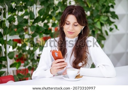 A beautiful young woman sits in headphones and speaks on a smartphone, online communication, work with gadgets, social distance, work online.
