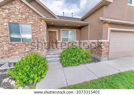 Facade of a house with shrubs, brown stone veneer siding, and garage Royalty-Free Stock Photo #2073315401