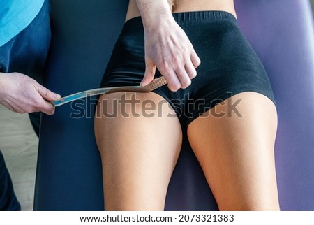 Osteopath is demonstrating Active release techniques ART or Soft tissue Release STR for the rectus femoris tendon with IASTM tool Royalty-Free Stock Photo #2073321383