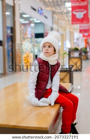 cute boy in a white fluffy hat in a shopping center against the background of bright lights