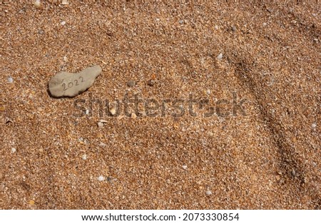 An image of the numbers of 2022 written on a pebble on the beach. The concept of New Year, Christmas and travel for winter holidays.