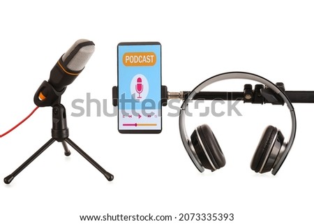 Modern microphone with headphones and mobile phone with podcast playlist on screen against white background