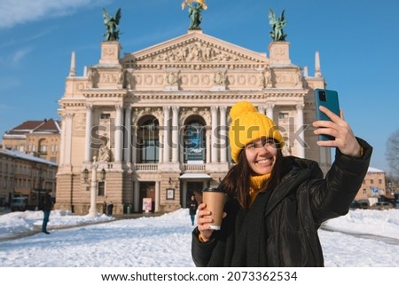woman traveler drinking coffee to go taking selfie in front of opera building lviv city ukraine
