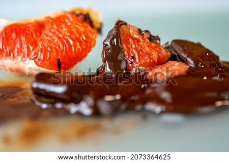 Dissolved bitter chocolate with pieces of sweet red grapefruit, closeup.