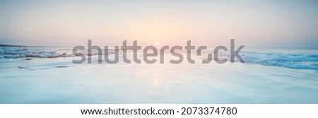 Panoramic view of the snow-covered shore of the frozen Baltic sea at sunset. Ice fragments close-up. Colorful cloudscape, soft sunlight. Symmetry reflections on the water. Christmas, seasons, winter Royalty-Free Stock Photo #2073374780