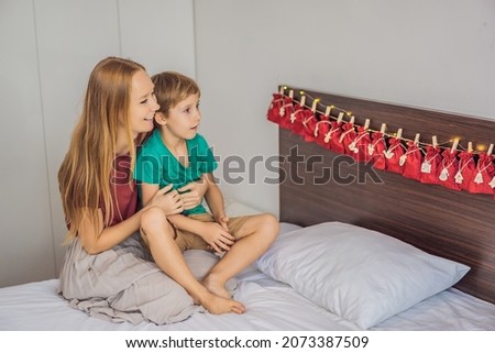 Smiling boy sitting on a bed opening first present from advent calendar. Winter seasonal tradition. Copy space
