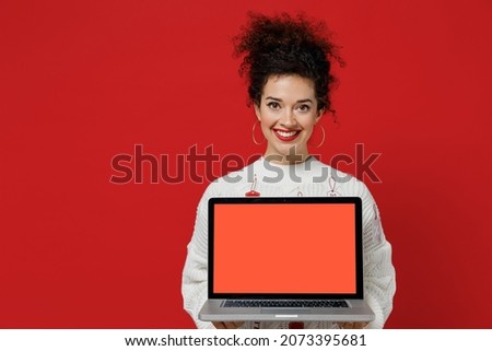 Young female costumer woman 20s wear white knitted sweater with tags sale in store showroom hold use work on laptop pc computer with blank screen workspace area isolated on plain red background studio