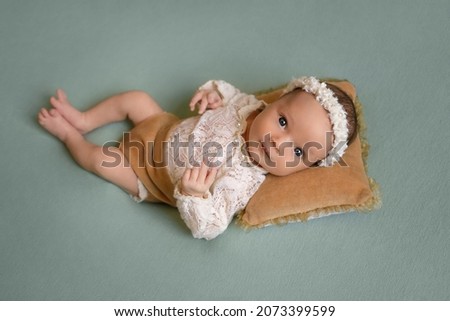 a newborn blue-eyed girl is lying on her back on a pillow on a green background