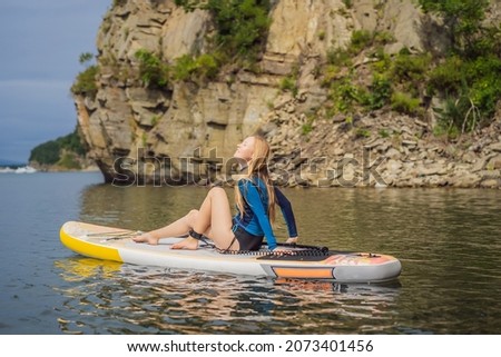 Young women Having Fun Stand Up Paddling in the sea. SUP. Red hair girl Training on Paddle Board near the rocks