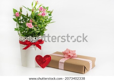 Bouquet of roses in white vase, valentine card and gift in wrapping paper on white background.