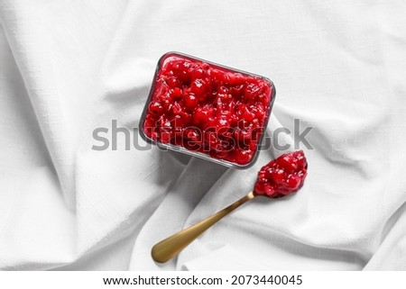 Bowl and spoon of tasty red currant jam on fabric background
