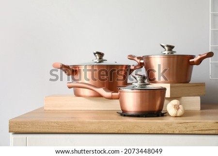 Set of copper cooking pots with garlic on counter near light wall Royalty-Free Stock Photo #2073448049