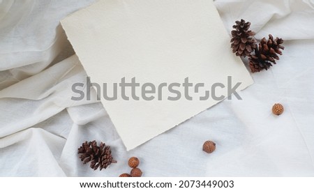 Photostock wedding styled composition. Feminine square recycled paper mockup scene with pinecone on white textured fabric background. side wiew