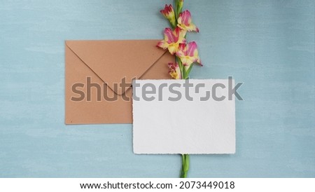 Photostock wedding styled composition. Feminine paper mockup scene with Amaryllis flower, silk ribbon, brown envelope, blank greeting card on Tosca textured concrete background. Flat lay, top view