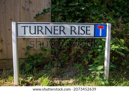 Turner Rise street name sign on two posts with shrubs and a wooden fence in the background
