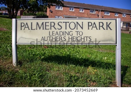Palmerston Park street name sign on two posts with grass and buildings in the background