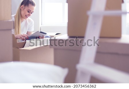 A beautiful single young woman unpacking boxes and moving into a new home. A women look at here tablet