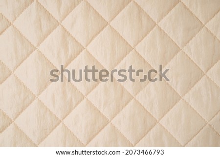 Quilted fabric background. Beige  texture blanket or puffer jacket  Royalty-Free Stock Photo #2073466793