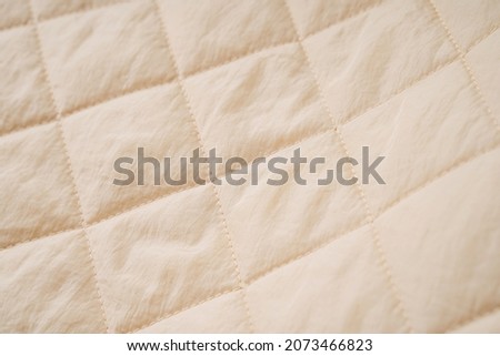 Quilted fabric background. Beige  texture blanket or puffer jacket 