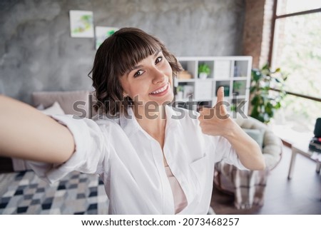 Self-portrait of attractive cheerful girl freelancer showing thumbup good solution at home loft brick interior indoors